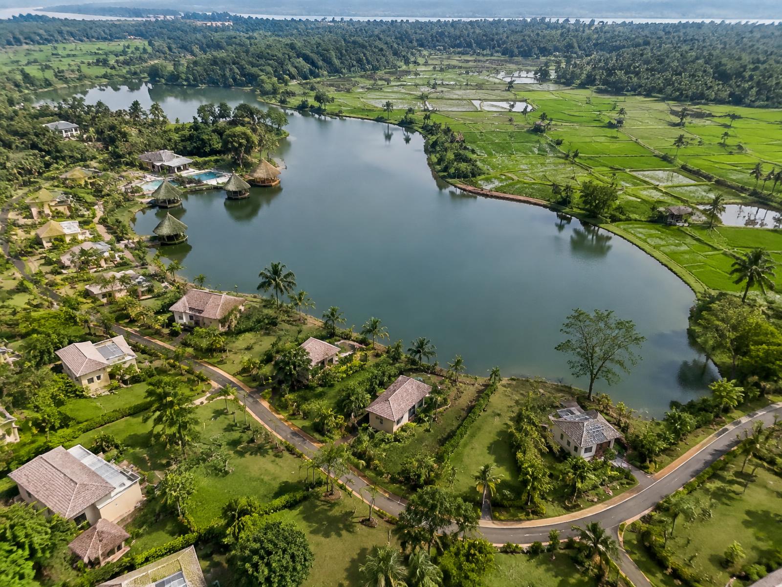 Vue aérienne du village : lac central, villas et bungalows séparés d'un côté, bas-fonds rizicoles de l'autre côté du lac